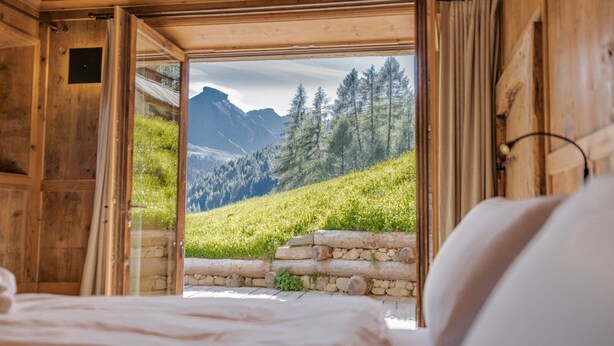 A wooden cabin room with a bed and a large window offering a view of a mountainous landscape.