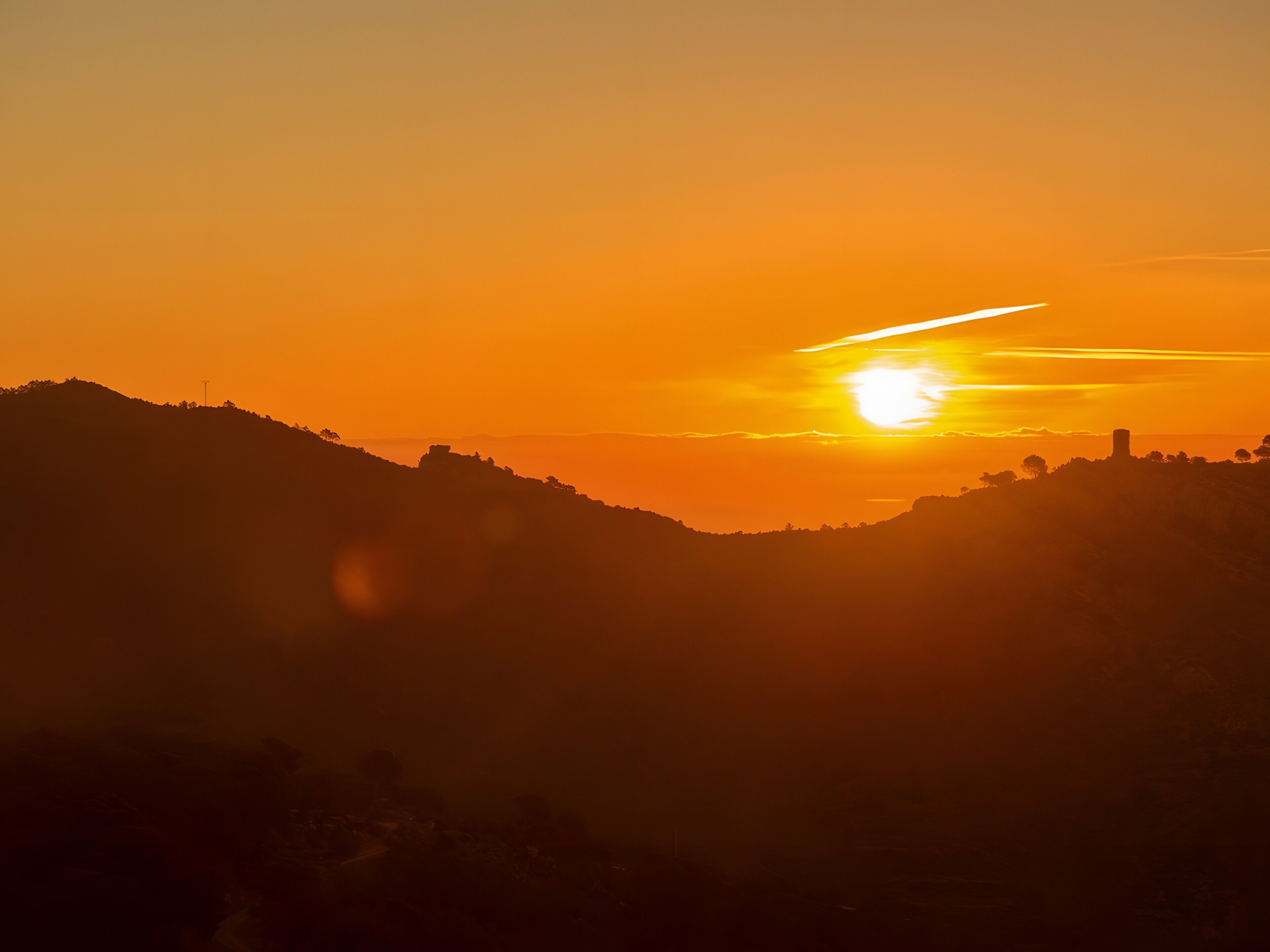 Un atardecer sobre un paisaje montañoso con la silueta de un edificio.
