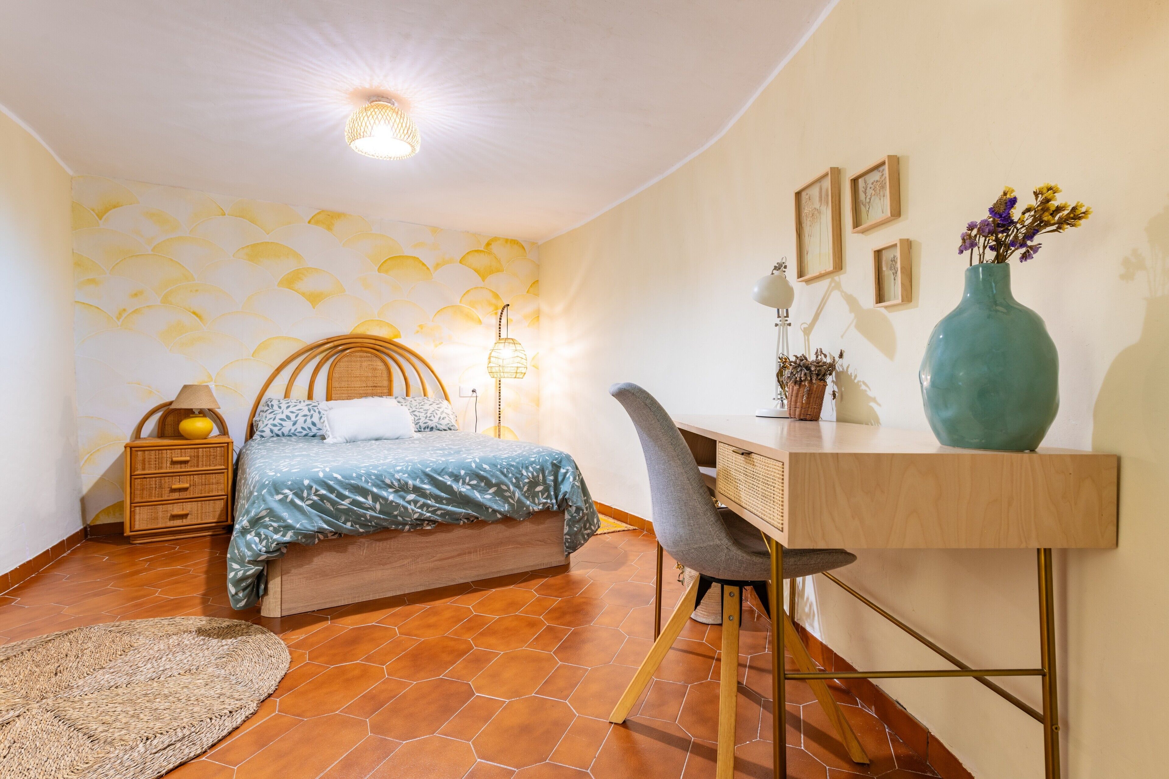 Een slaapkamer met een bed, bureau, stoel, lamp en wanddecoratie.