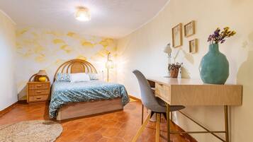 Een slaapkamer met een bed, bureau, stoel, lamp en wanddecoratie.