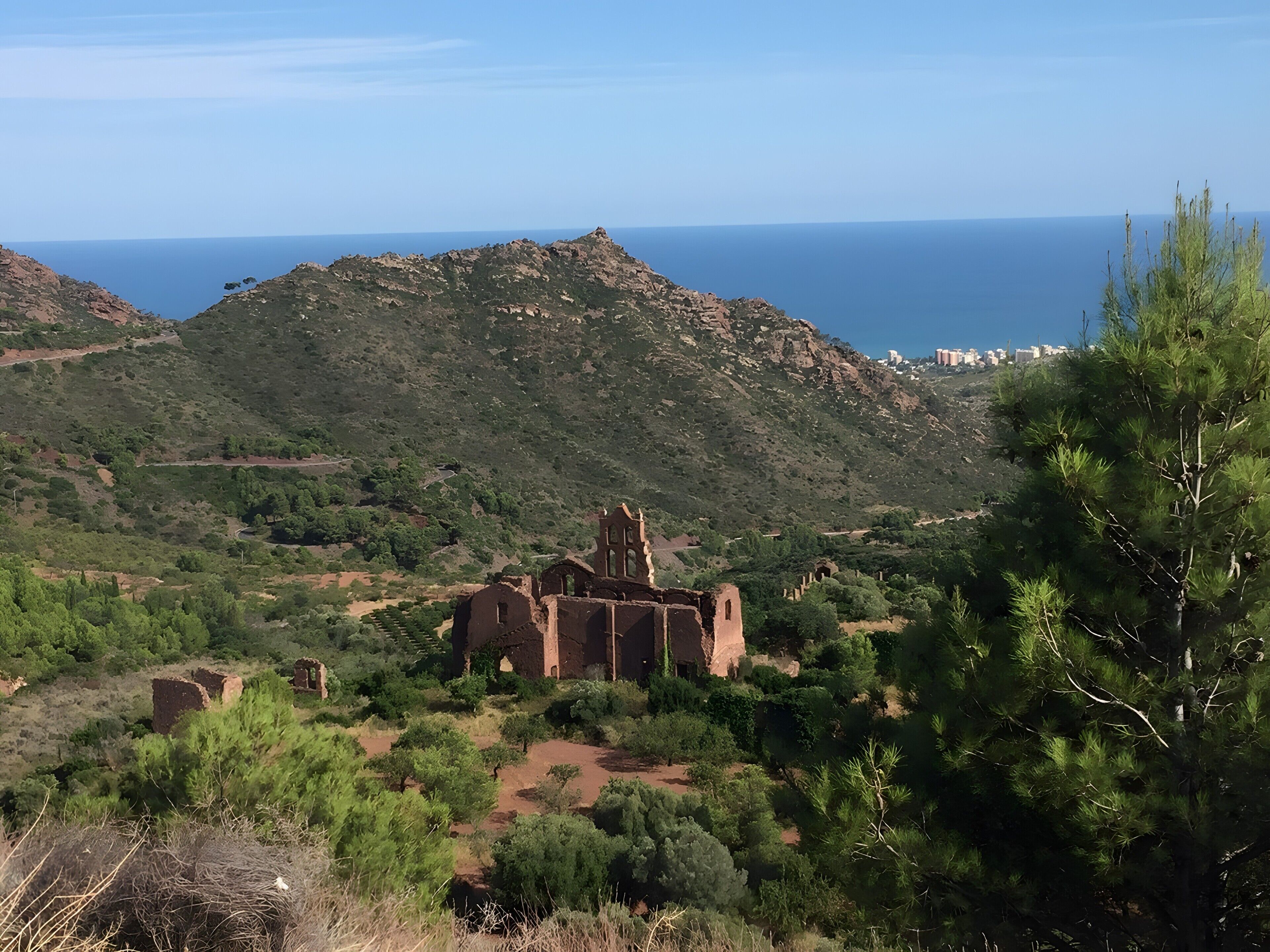 A historical building with ruins, surrounded by greenery and overlooking a coastal landscape.