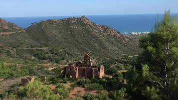 A historical building with ruins, surrounded by greenery and overlooking a coastal landscape.