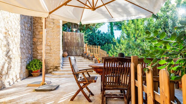 An outdoor patio with a stone wall, wooden chairs, a table, and a large umbrella. - Casa en las Montañas de Benicassim — Mountain Forest Retreat with Private Terrace and Wi-Fi (Benicassim)