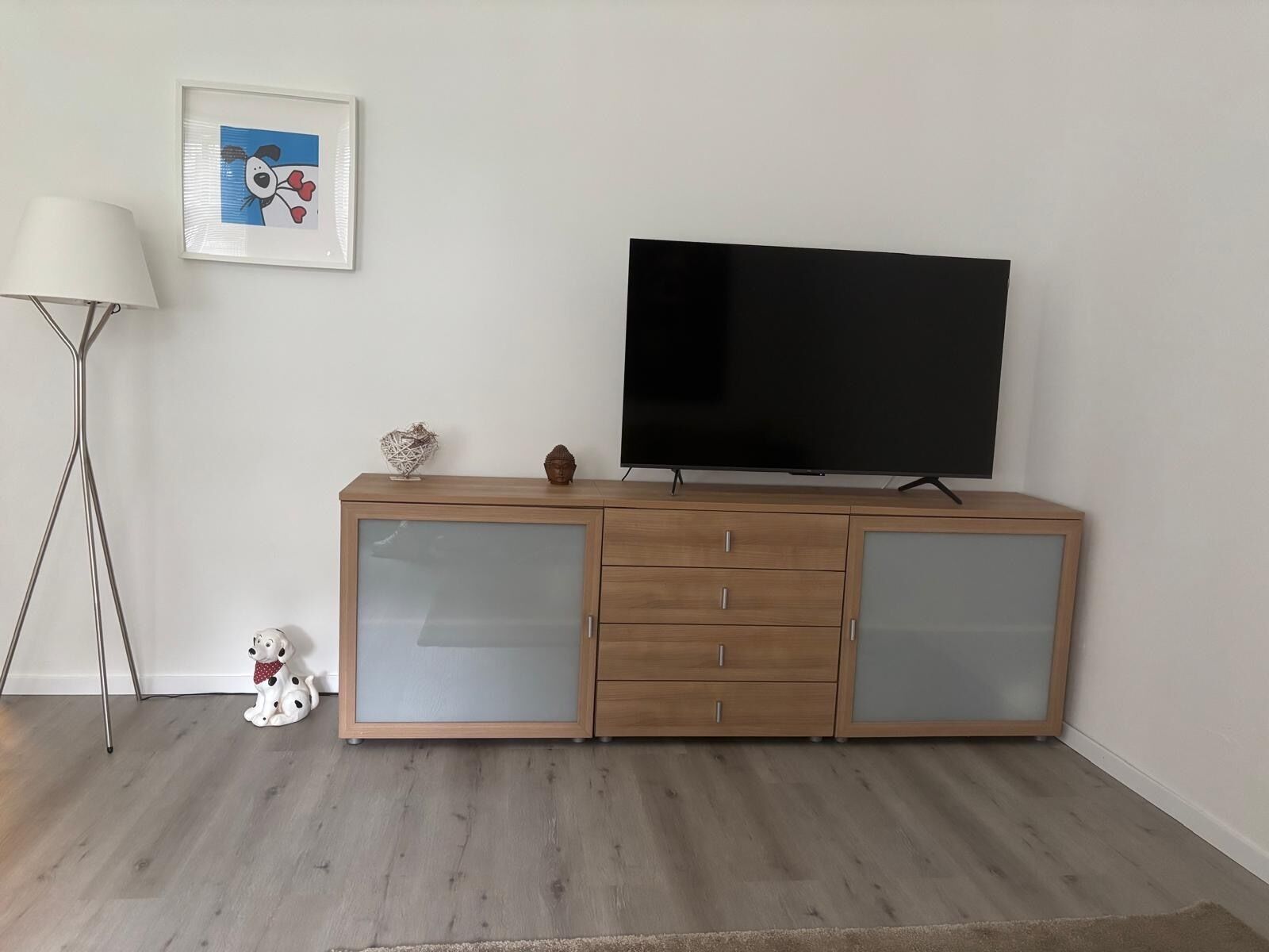 Un meuble en bois pour la télévision, sur lequel est posée une télévision à écran plat, ainsi qu’un tableau encadré et une lampe sur pied.