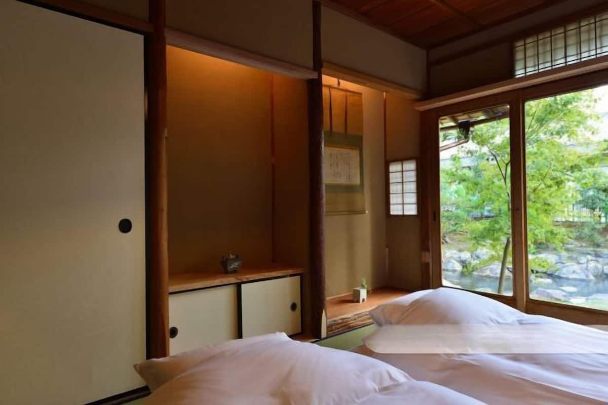 Um quarto tradicional japonês com tatames, uma porta deslizante e vista para um jardim através de uma grande janela.