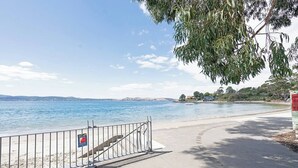 Un paseo marítimo con barandilla metálica, vista despejada al mar y una costa distante con edificios.
