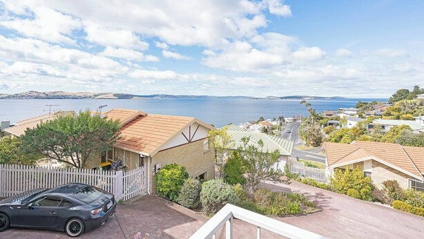 Un área residencial costera con casas, un coche estacionado y vista al mar.