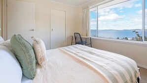 Un dormitorio con cama, una silla, un ventanal con vistas al mar y una puerta.