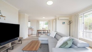 Una sala moderna con televisor de pantalla plana, una mesa de centro de madera, un sofá gris y un comedor con mesa y sillas.