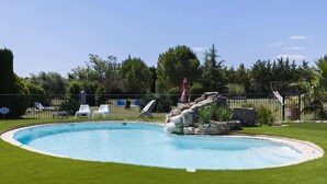Une piscine agrémentée d’un élément rocheux, entourée d’une pelouse bien entretenue et d’une clôture.