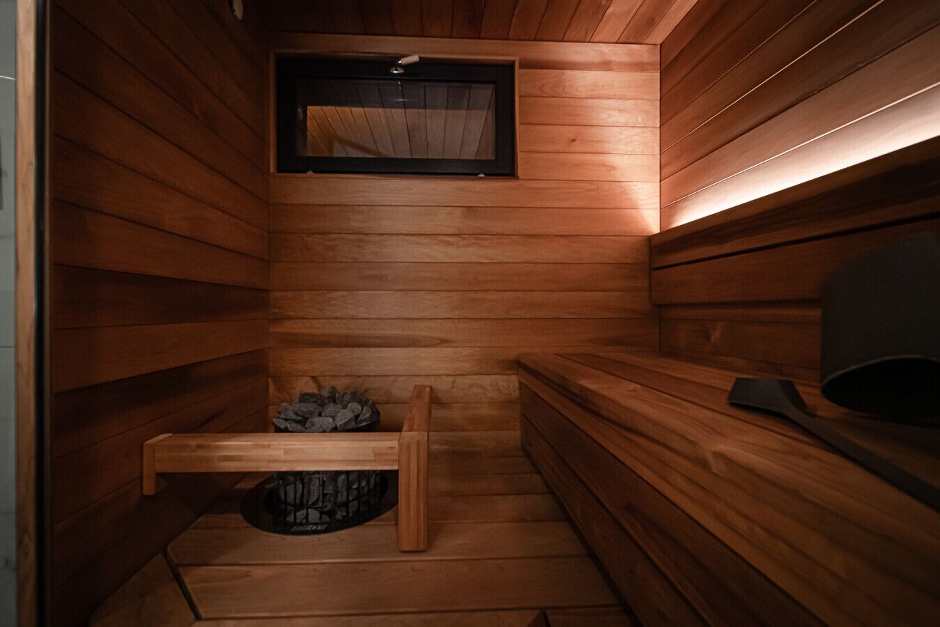 A sauna with wooden walls, a bench, a small table with a towel, and a window.
