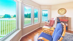 A room with large windows, a wooden chair, a small table, and a bookshelf. - 2bd, 2ba, Walk to Town and Beach (SRetreat) (Long Beach)