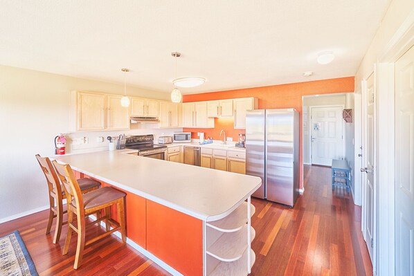 A modern kitchen with a central island, wooden chairs, and a stainless steel refrigerator.