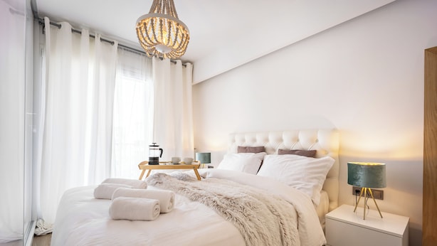 A neatly made bed with a fluffy blanket and towels, a bedside table with a lamp, and a chandelier. - Luxury 3-Bedroom Apartment Athens Nea Smirni (ΝΕΑ ΣΜΥΡΝΗ)