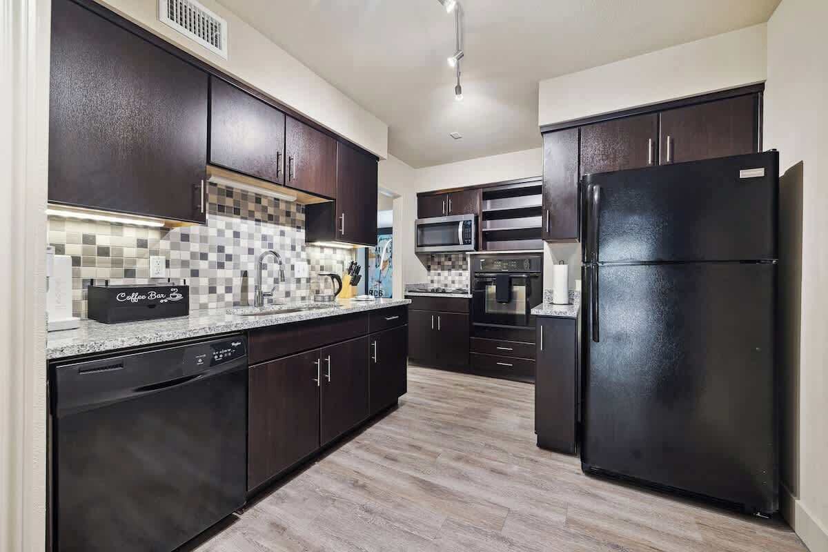A modern kitchen with dark cabinets, a black refrigerator, and a coffee bar.