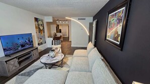 A modern living room with a flat-screen TV, a sofa, a coffee table, and artwork on the walls.