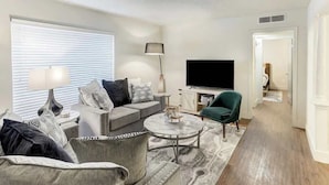 A modern living room with a grey sofa set, a round coffee table, and a flat-screen TV.