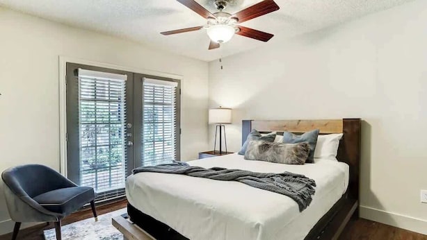 A bedroom with a bed, a chair, a ceiling fan, and a window with blinds.