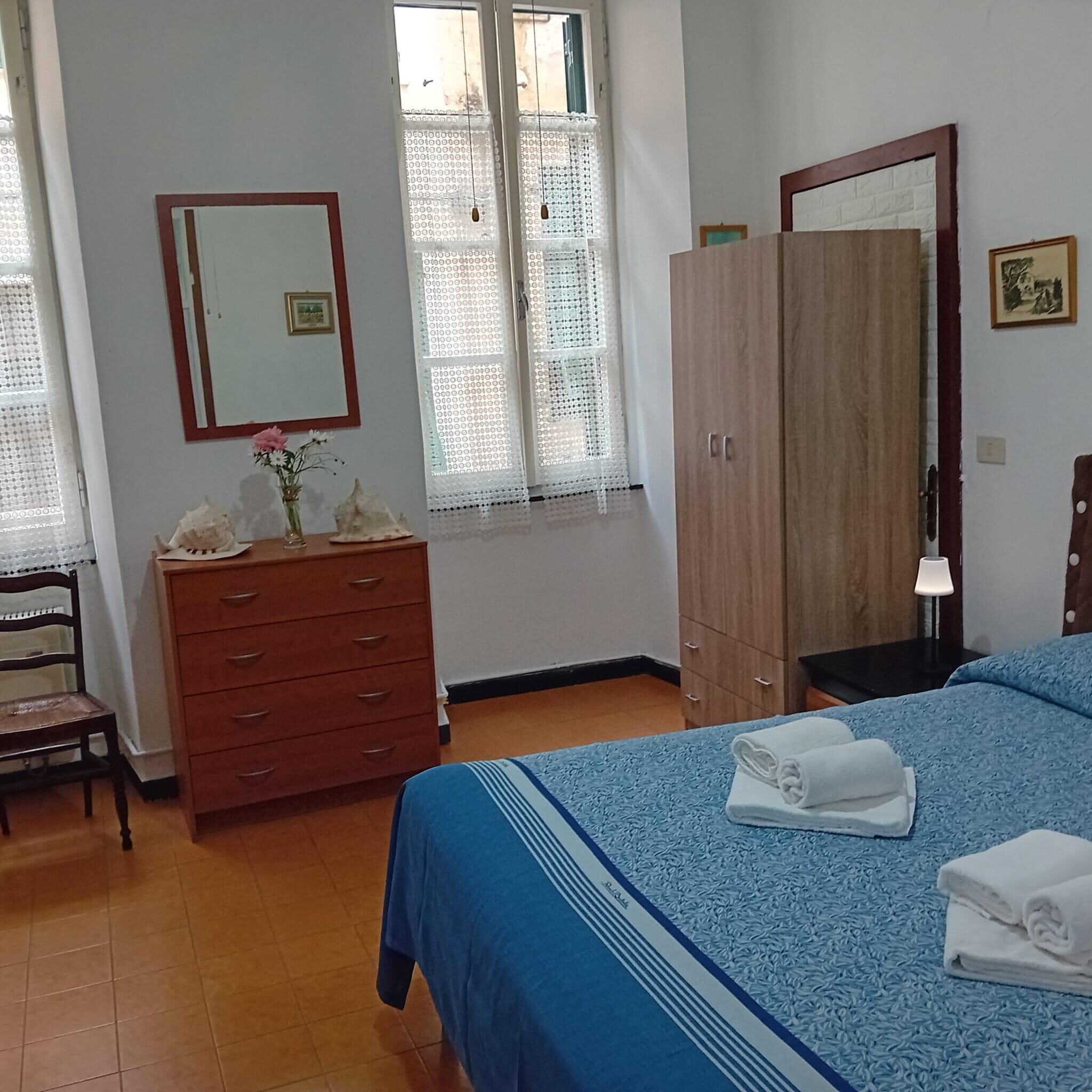 Ein Schlafzimmer mit einem Bett, einem Holzschrank, einem Schminktisch, einem Spiegel und einem Fenster mit Spitzenvorhängen.
