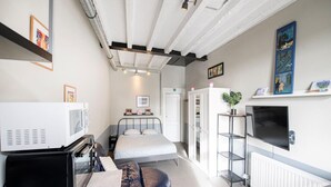 A compact hotel room with a bed, a desk, a television, and a kitchenette.