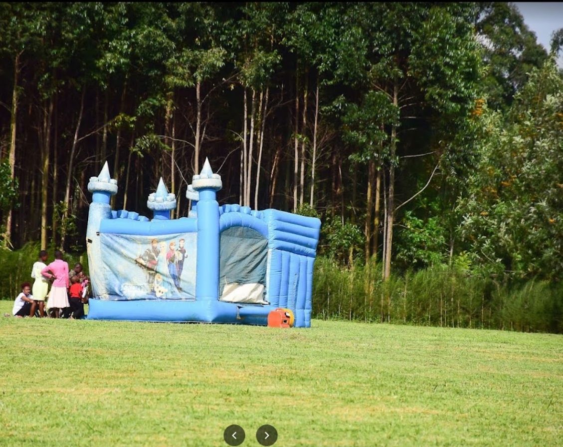 Uma estrutura inflável azul para brincar em um campo gramado, com árvores ao fundo.