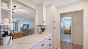 Una cocina moderna con armarios blancos, encimera de mármol y vista al comedor.