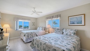 A bedroom with two beds, a ceiling fan, a window with a view, and a framed picture on the wall.