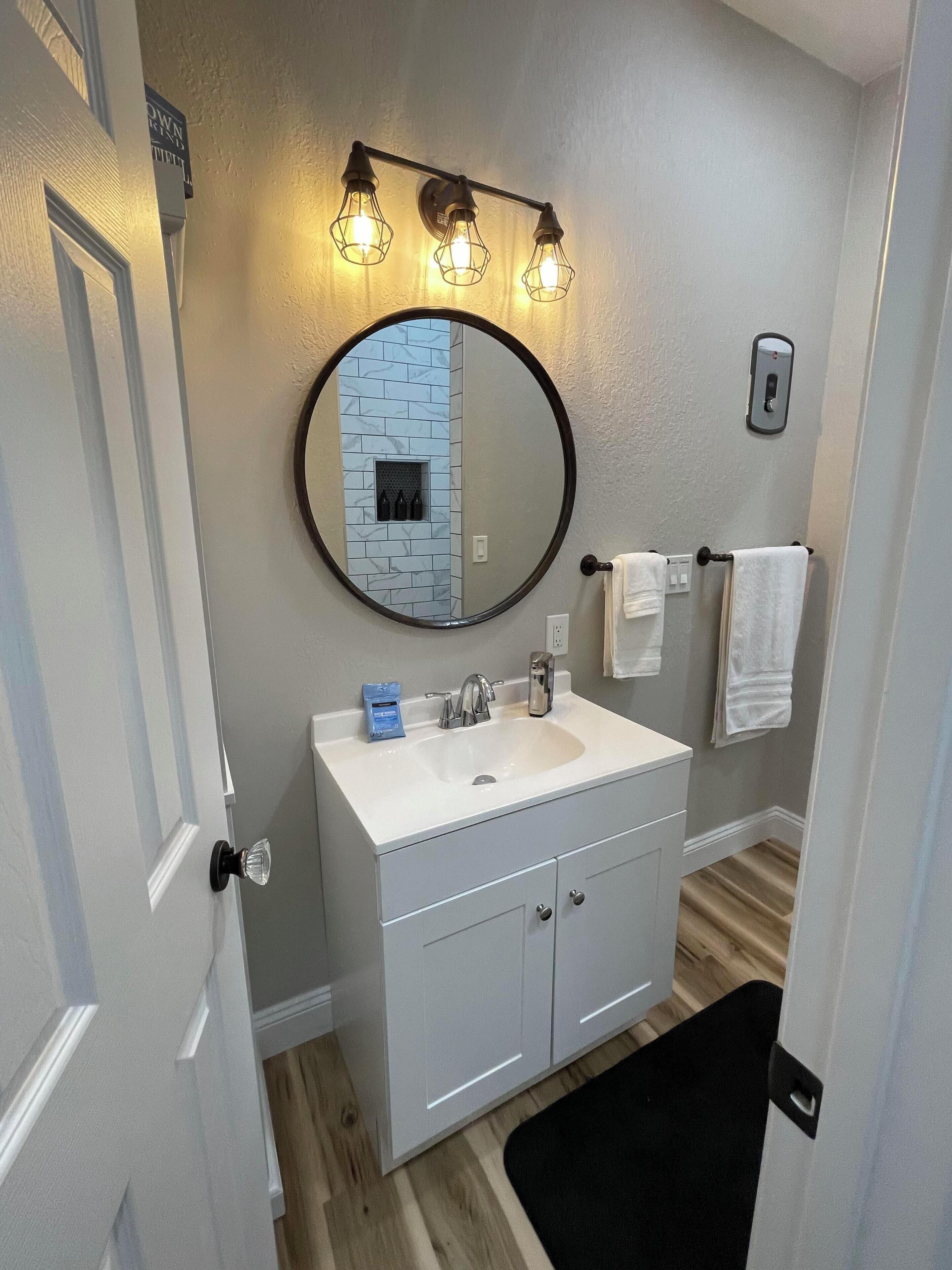 Une salle de bain avec un meuble-lavabo blanc, un miroir rond et un luminaire placé au-dessus du miroir.