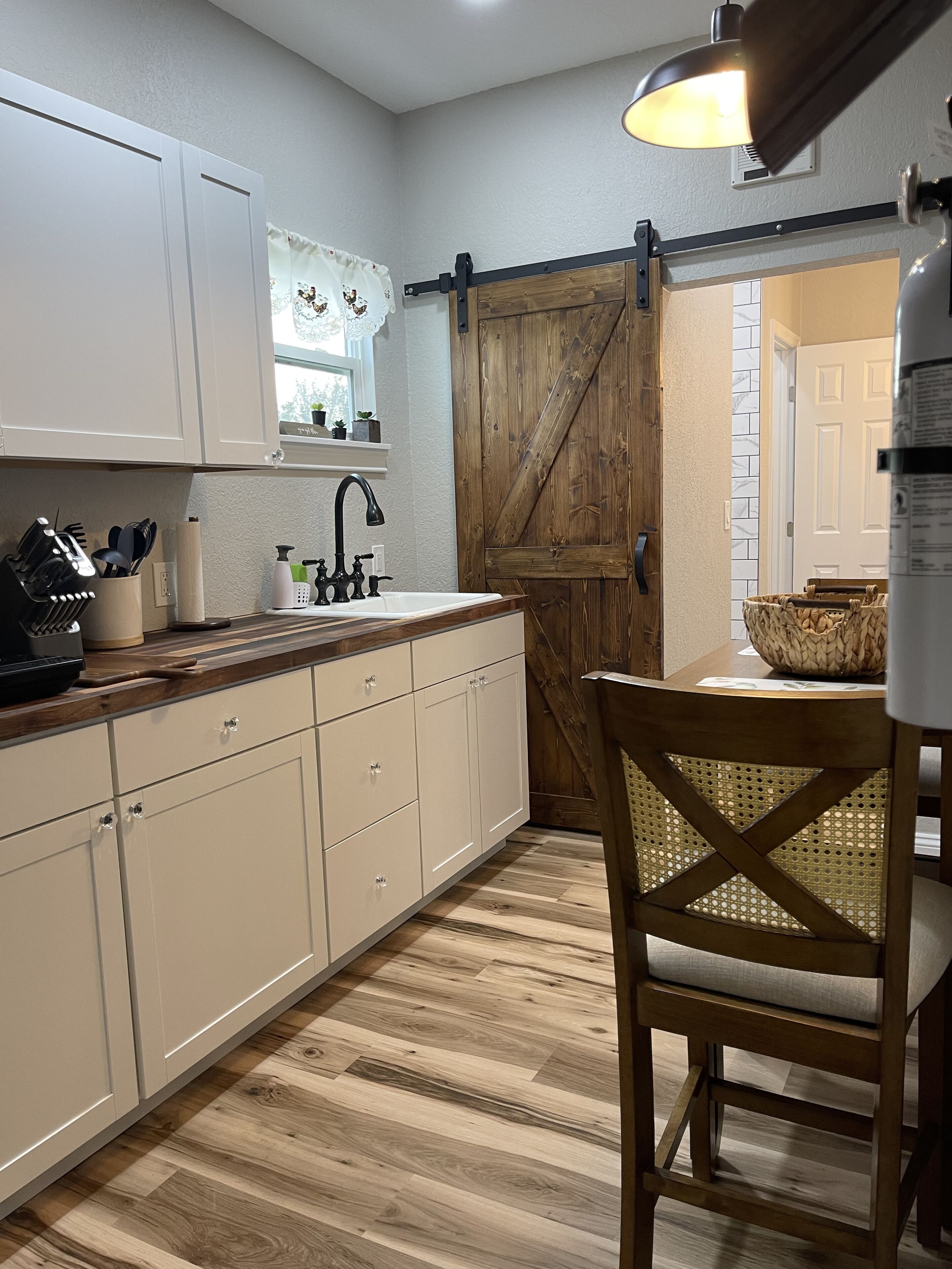 A kitchen with white cabinets, a wooden countertop, a sink, and a dining area with a chair and table.