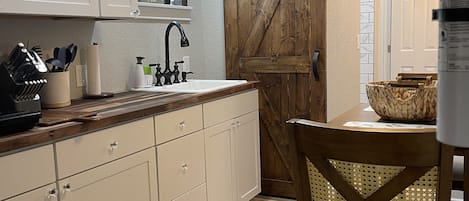 A kitchen with white cabinets, a wooden countertop, a sink, and a dining area with a chair and table.
