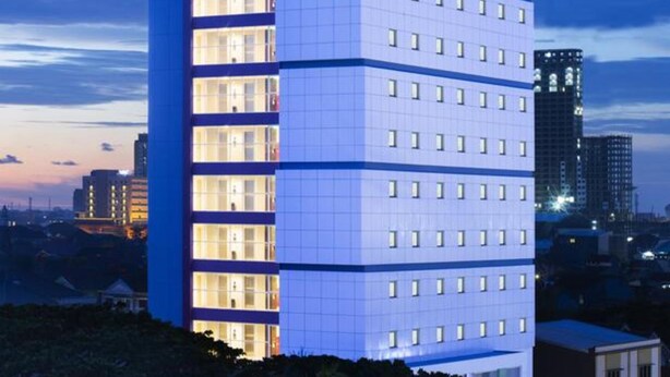 Et moderne hotel med flere etager, med et markant rødt logo øverst.
