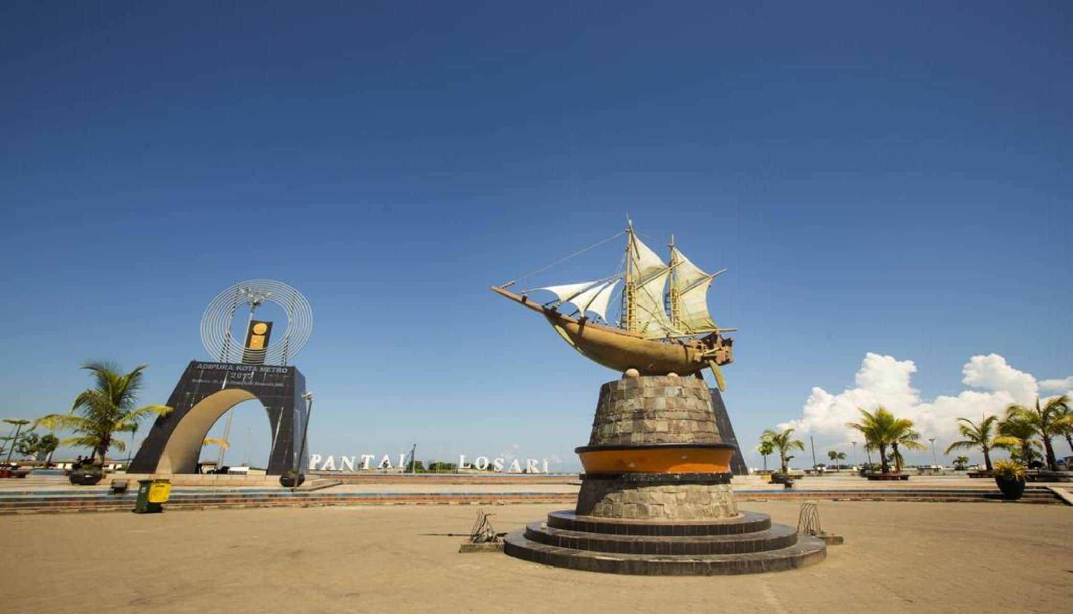 Une zone côtière où se trouve une grande sculpture représentant un navire, une arche et un panneau indiquant « PANTAI LOSARI ».