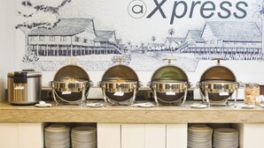En buffetopstilling med fire store metalfade, en skraldespand og en kaffemaskine på en bordplade.