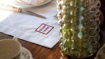 Una mesa con servilleta blanca, un florero de cristal con flores, una taza y un plato con fruta.