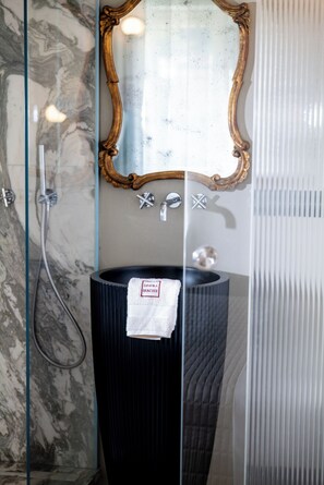 A bathroom with a marble wall, a glass shower enclosure, a black sink with a towel, and a gold-framed mirror. - Dimora Moncher (Capanne-Prato-Cinquale)
