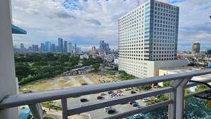 A cityscape with a prominent white building with blue windows, surrounded by other high-rise buildings and greenery. - Cozy Corner: Pet-Friendly 1BR with Sweeping City View (Taguig)