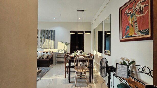 A dining area with a table set for six, a sofa, and a large mirror. - Cozy Corner: Pet-Friendly 1BR with Sweeping City View (Taguig)