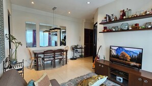 A modern living room with a dining area, a TV, and shelves with decorative items. - Cozy Corner: Pet-Friendly 1BR with Sweeping City View (Taguig)