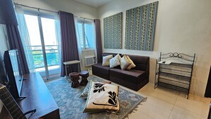 A living room with a sofa, a coffee table, a TV, and a window with curtains. - Cozy Corner: Pet-Friendly 1BR with Sweeping City View (Taguig)