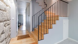 Una escalera de madera con barandillas negras que conduce a una habitación con pared de piedra y una puerta.