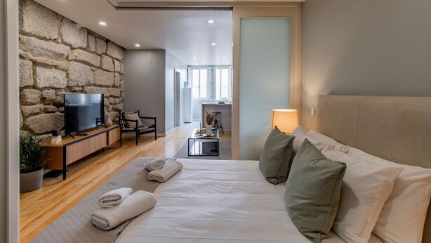 Un dormitorio moderno con pared de piedra, televisión, escritorio y cama con almohadas.