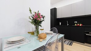 A modern kitchen with black cabinets, a glass dining table, and a vase with flowers. - Italianway Easy - Ponte Seveso 25 (Milan)