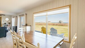 A dining area with a large window, wooden walls, and outdoor seating visible. - Shore to Sky Oceanfront Escape with Sunroom, Stunning Views & Beach Access (Prince Edward Island)