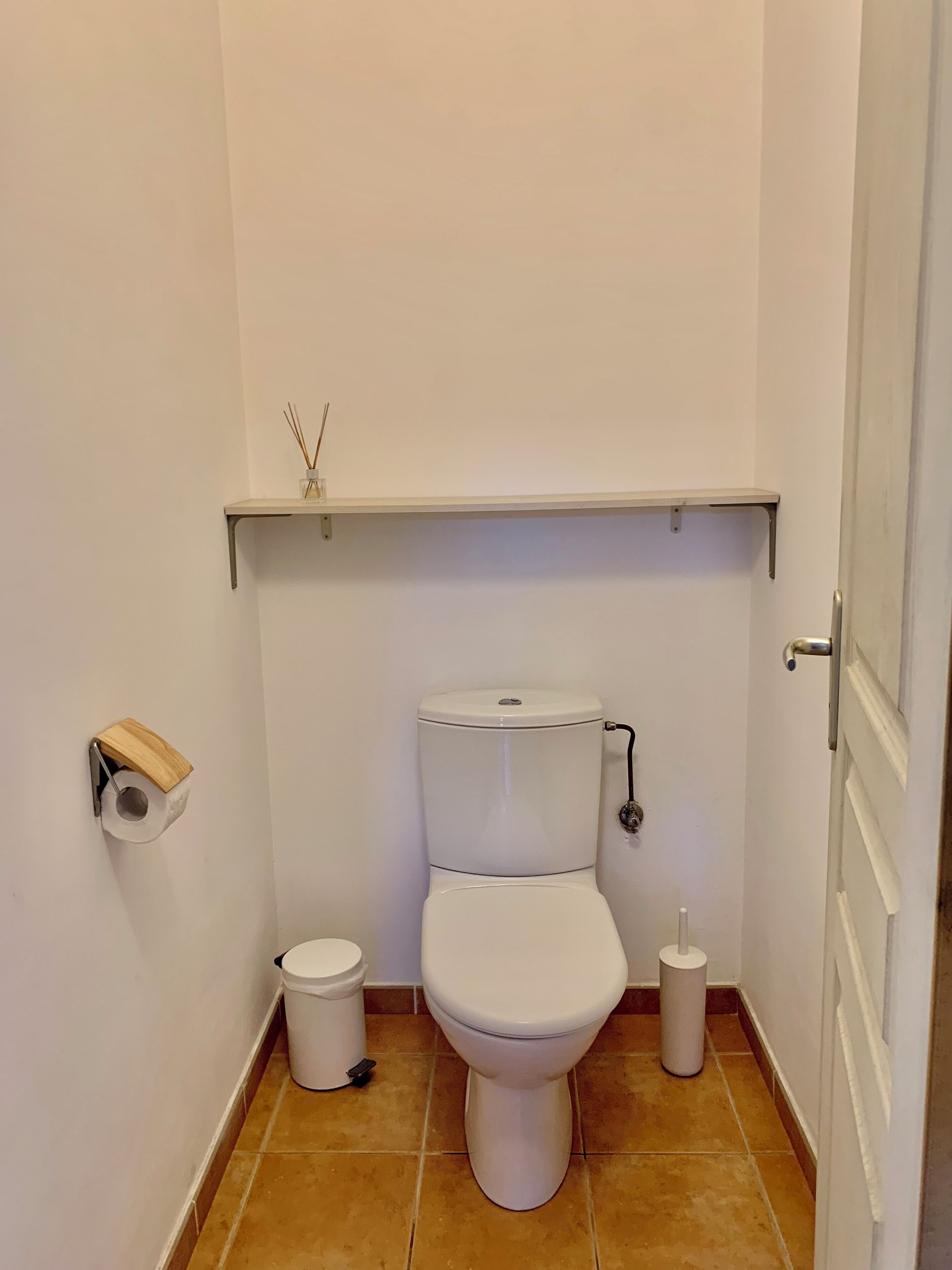 A small, clean bathroom with a toilet, a trash bin, and a toilet paper holder.
