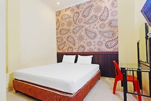 A hotel room with a bed, a red chair, and a patterned wallpaper.