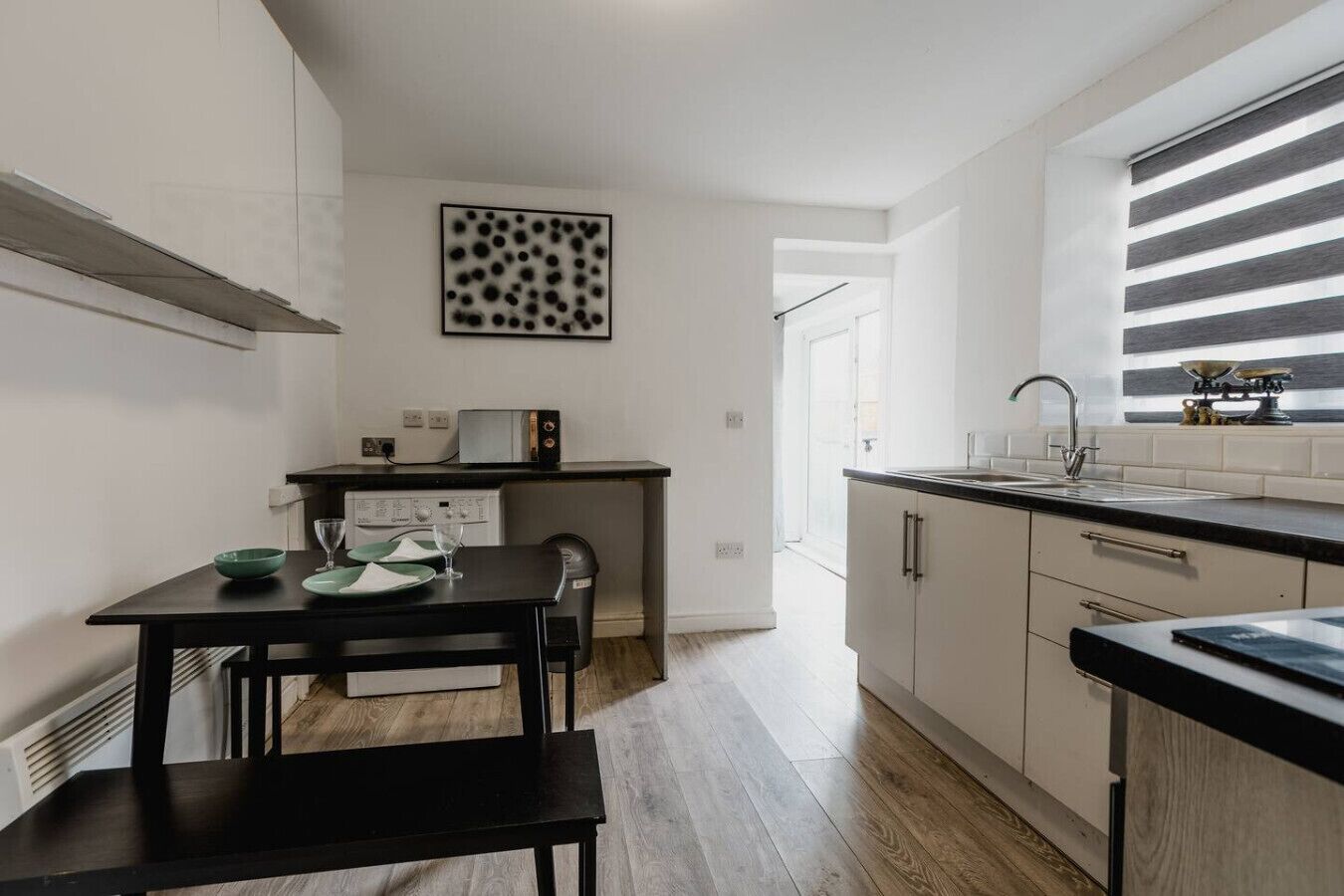 Une cuisine compacte comprenant une table à manger, un four à micro-ondes et une fenêtre équipée de stores horizontaux.