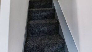 A narrow, carpeted staircase with white walls and a door at the top.