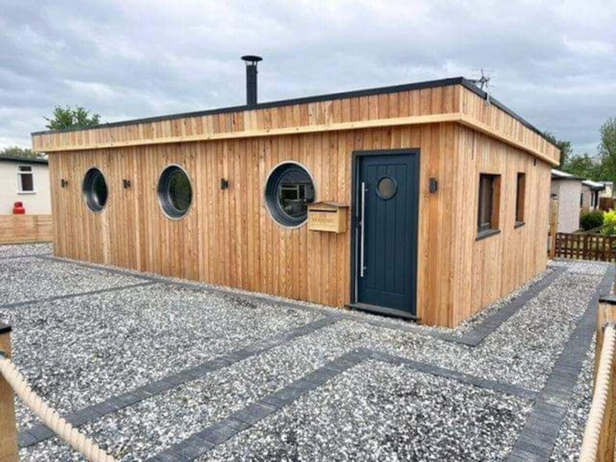 Un bâtiment en bois avec une porte bleu foncé, trois fenêtres rondes et une cheminée.
