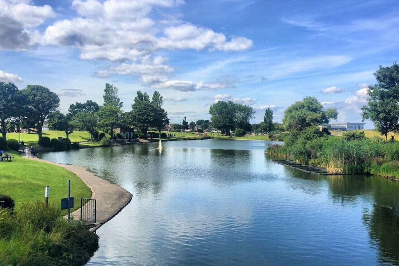 A serene riverside park with a walking path, trees, and a distant building.