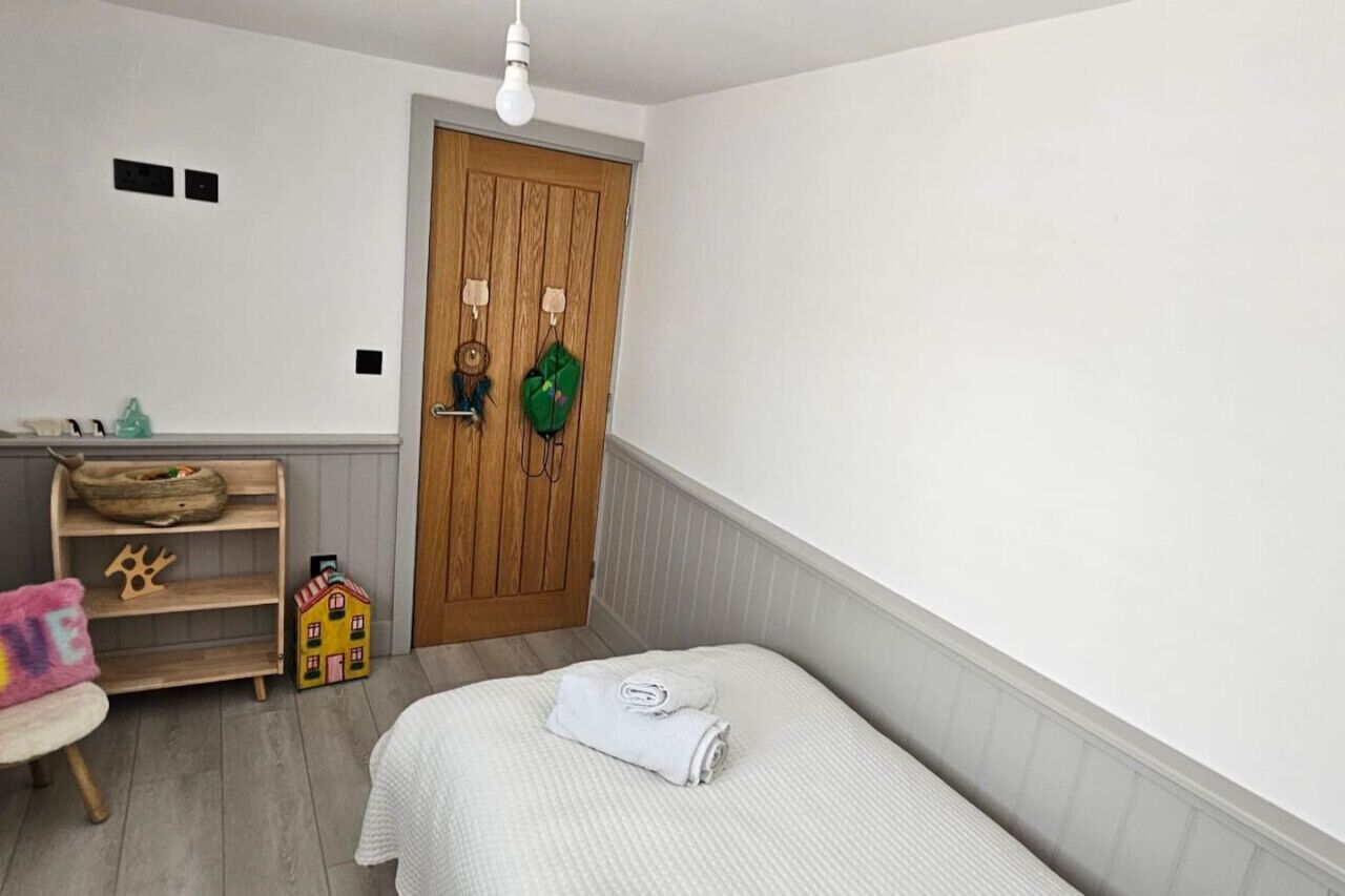 Un dormitorio con una cama, una puerta de madera, un estante con juguetes y una pequeña silla.